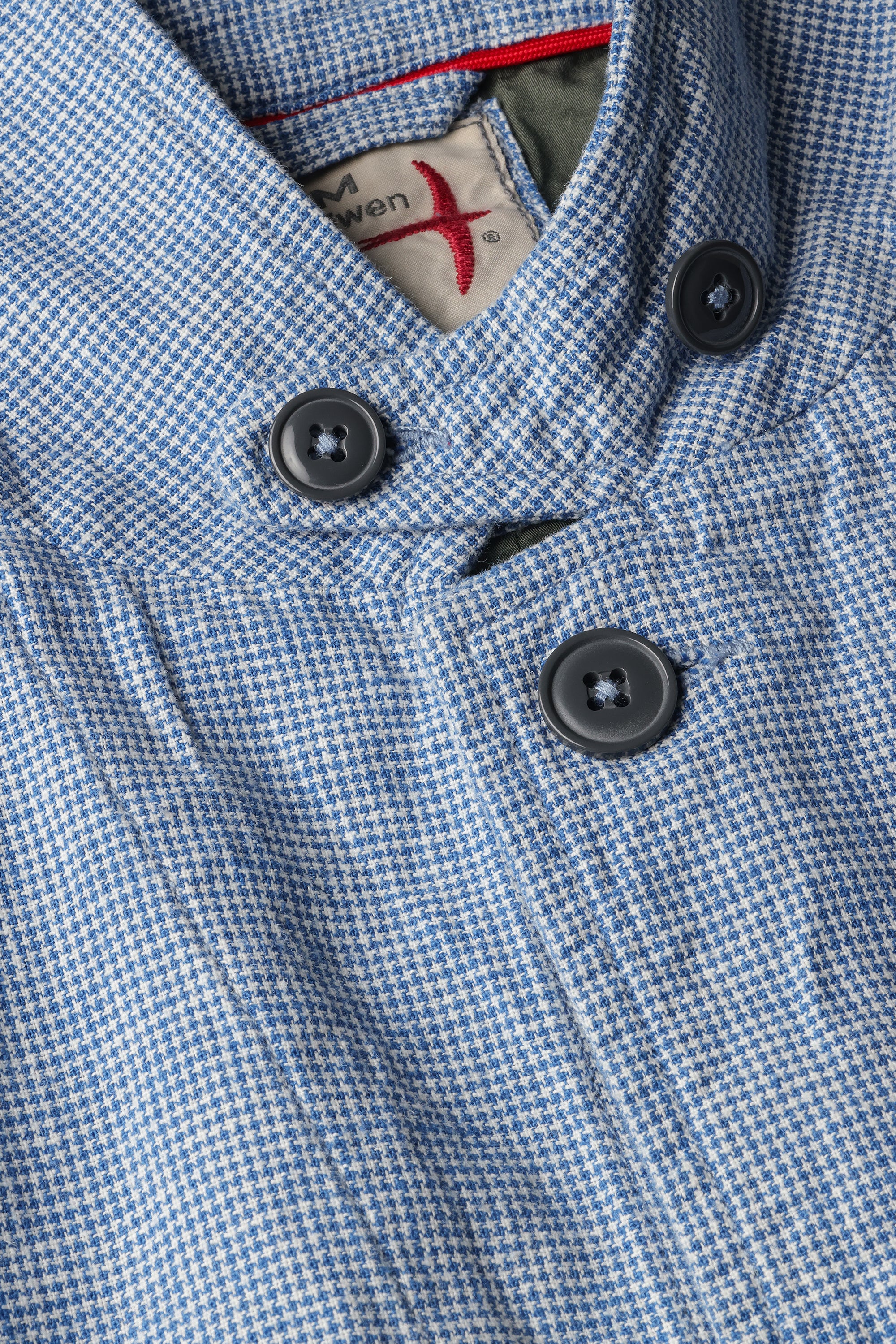 Close-up of a blue checkered coat with black buttons and a brand label.